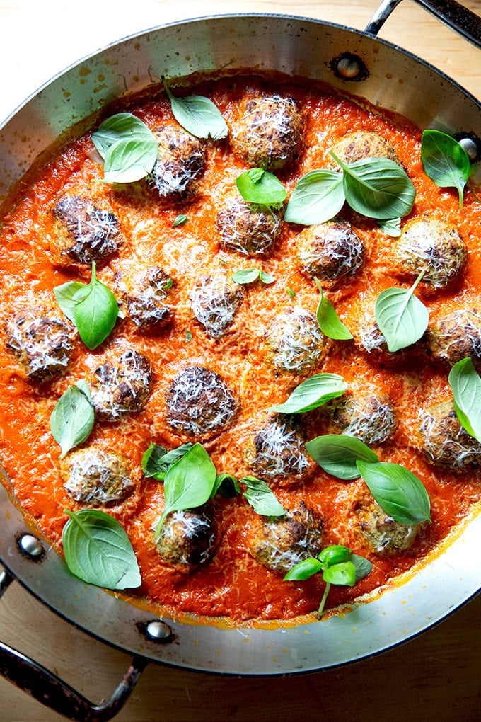 A skillet filled with tomato sauce, eggplant meatballs and fresh basil.