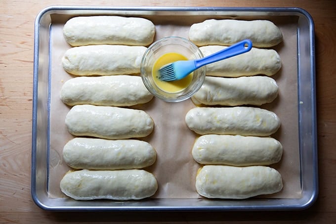 Brioche hot dog buns, unbaked, on a sheet pan, brushed with egg wash.