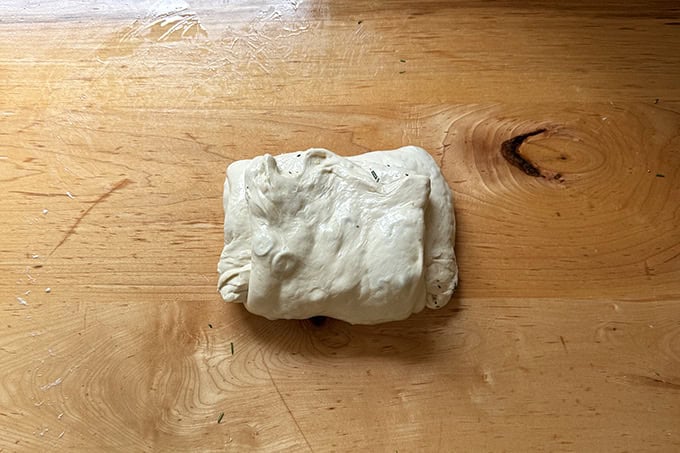 Final fold of a batch of rosemary-olive sourdough on a counter top.
