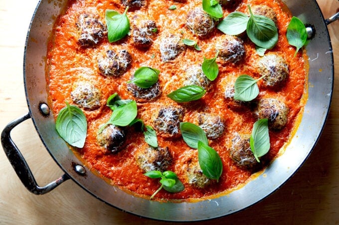 Eggplant meatballs in a skillet topped with fresh basil and parmesan.