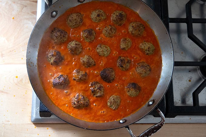 Eggplant meatballs simmering in tomato sauce on the stovetop.