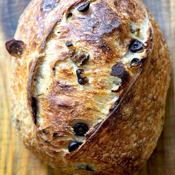 A freshly baked loaf of rosemary-olive sourdough bread on a wooden cutting board.
