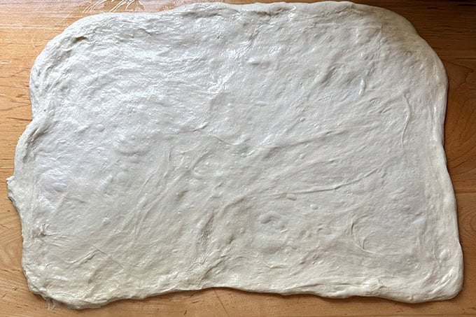 Sourdough dough stretched thinly across a counter top into a 20x15-inch rectangle.
