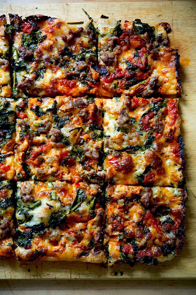 Just-baked grandma-style pizza, cut into squares on a cutting board.