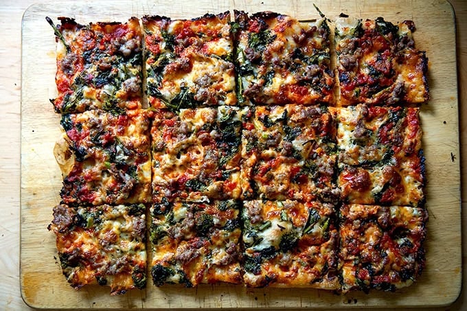 Just-baked grandma-style pizza, cut into squares on a cutting board.