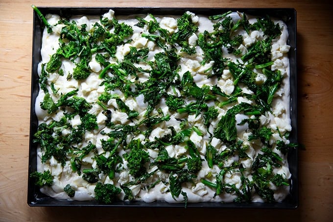 An unbaked grandma-style pizza topped with cheese and sautéed broccoli rabe.