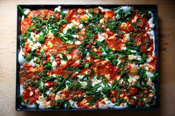 An unbaked grandma-style pizza topped with cheese, sauce, and sautéed broccoli rabe.