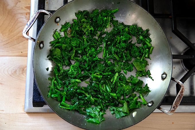 Sautéed broccoli rabe in a large skillet on a stovetop.