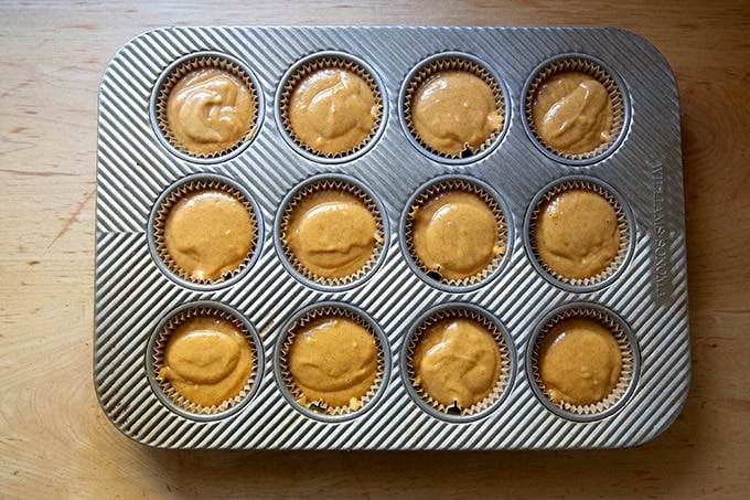 A 12-well muffin tin filled with pumpkin muffin batter.