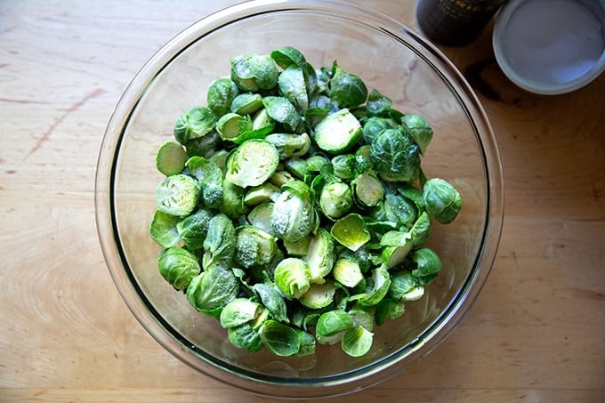 A bowl of halved Brussels sprouts seasoned with salt and olive oil.