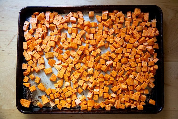 A sheet pan filled with cubes of sweet potatoes tossed with melted coconut oil, salt, and Aleppo pepper.