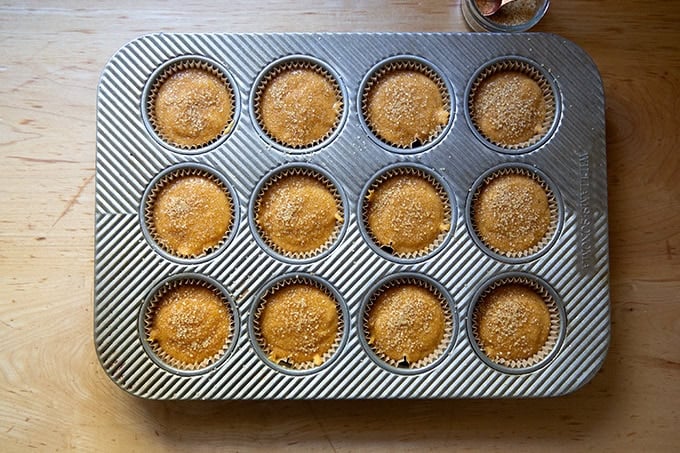 A 12-well muffin tin filled with pumpkin muffin batter topped with turbinado sugar.