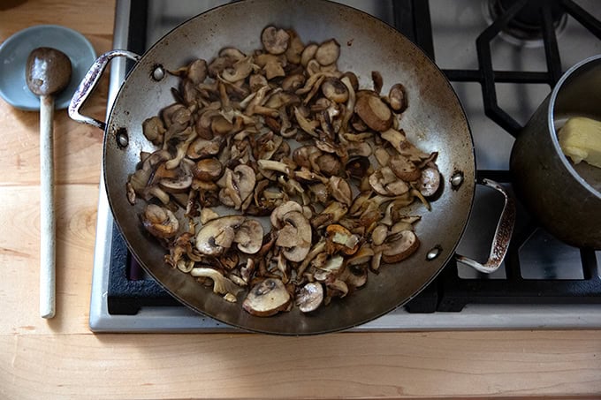 A large pan on the stovetop filled with sautéed mushrooms.