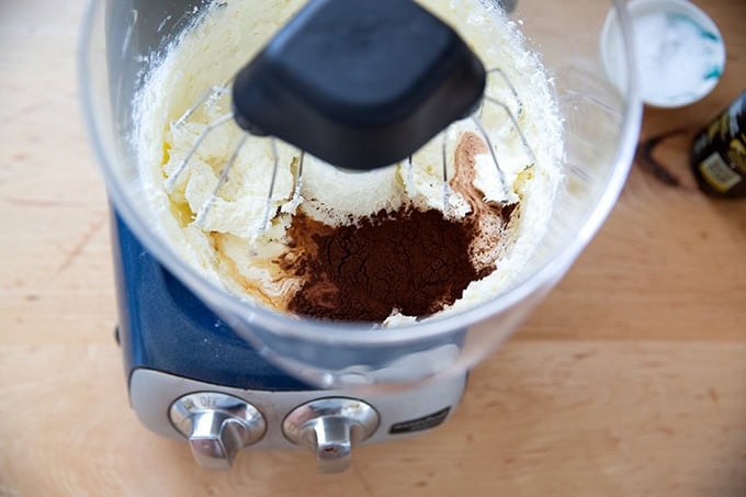 A stand mixer holding whipped sugar and cream cheese as well as cocoa powder, vanilla, salt, and heavy cream.