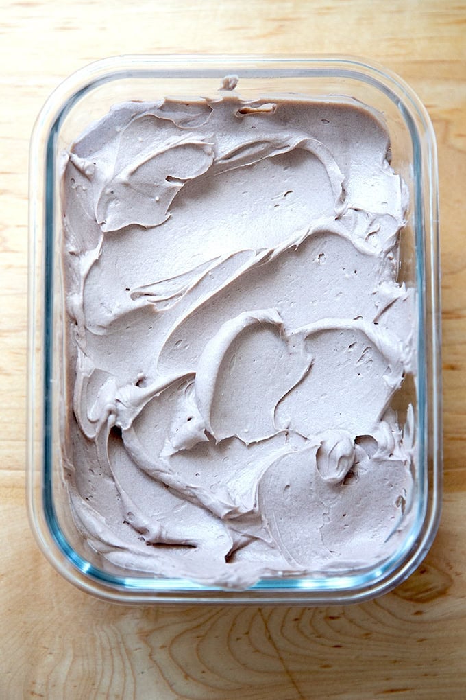 A glass storage container holding chocolate whipped cream cheese frosting.