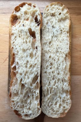 Giant sandwich roll dough, halved on a cutting board.
