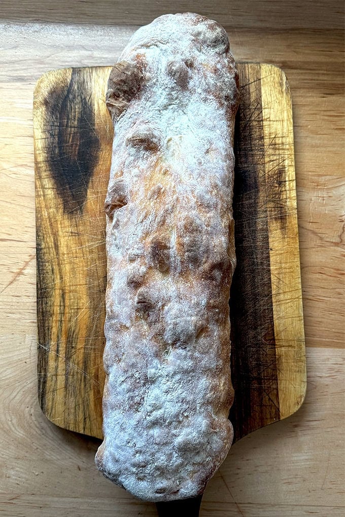 A just-baked giant sandwich roll on a cutting board.